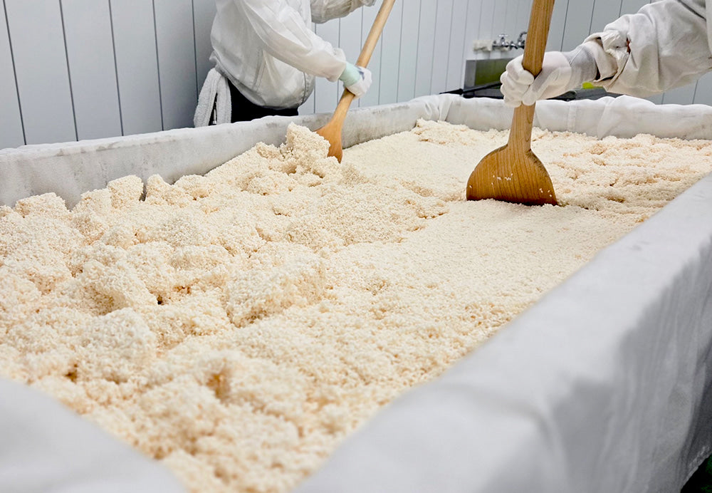 Worker stirring koji in a Japanese fermentation factory, demonstrating traditional umami production.